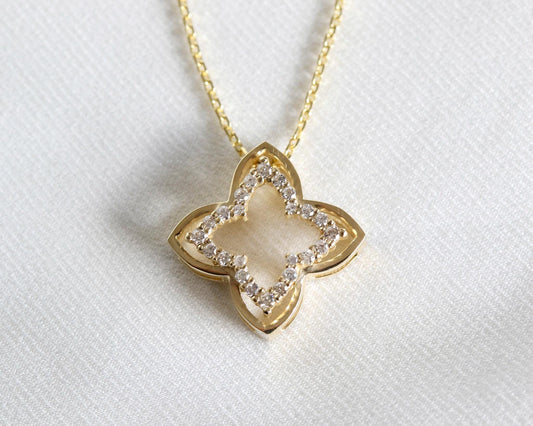 Close-up of a 14K yellow gold open four-leaf clover pendant with prong-set diamonds on white fabric