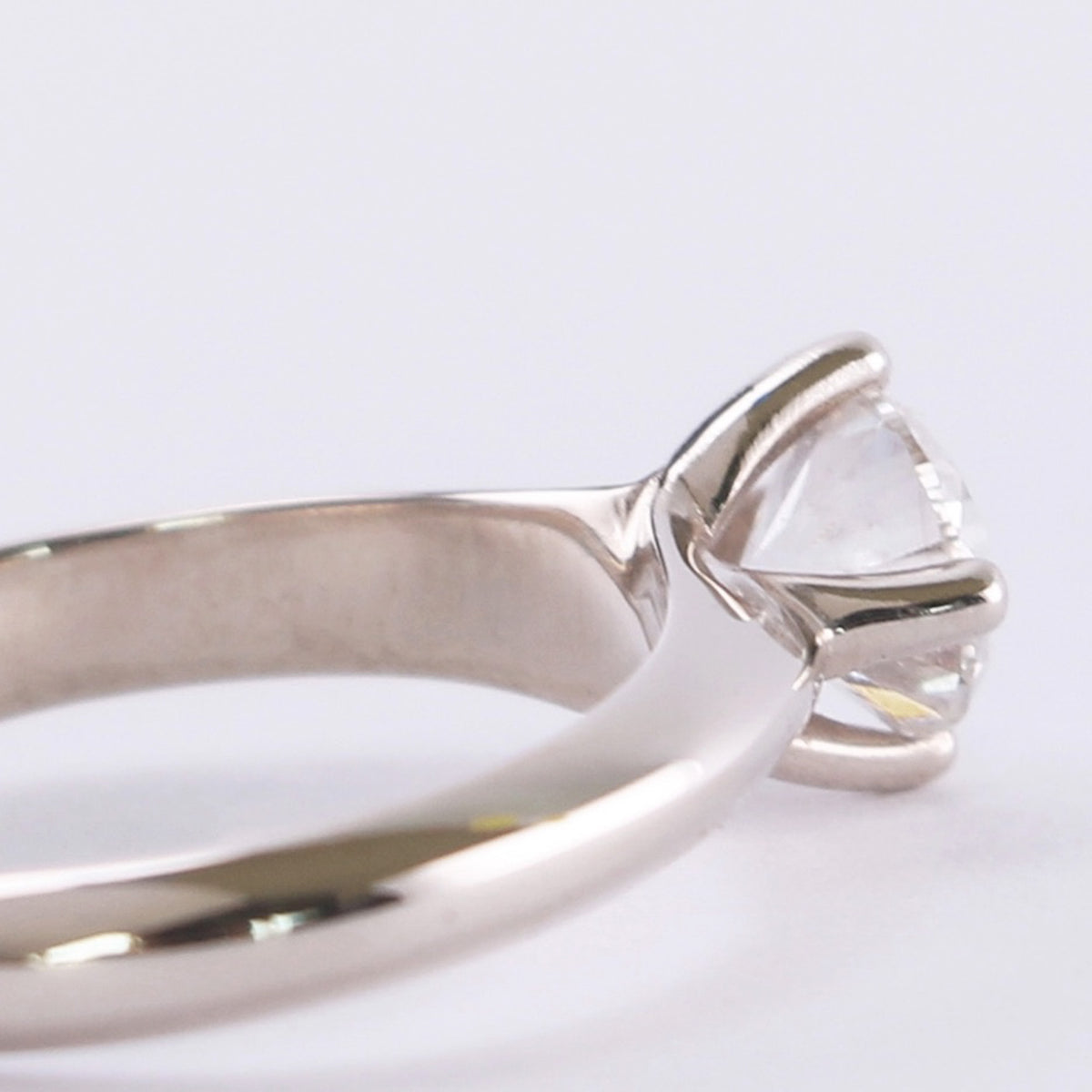 Close-up side view of a four-prong diamond setting rising out of a white gold band