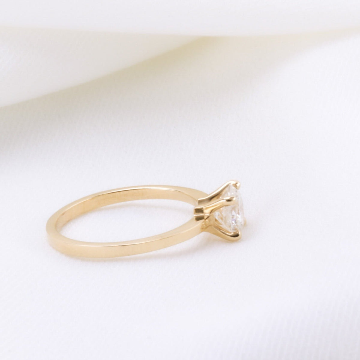 Side view of a four-prong diamond solitaire ring with a straight square-profile gold band