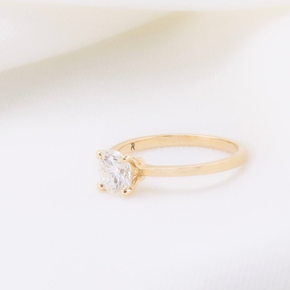 Four-prong round diamond solitaire on a straight yellow gold band, angled view