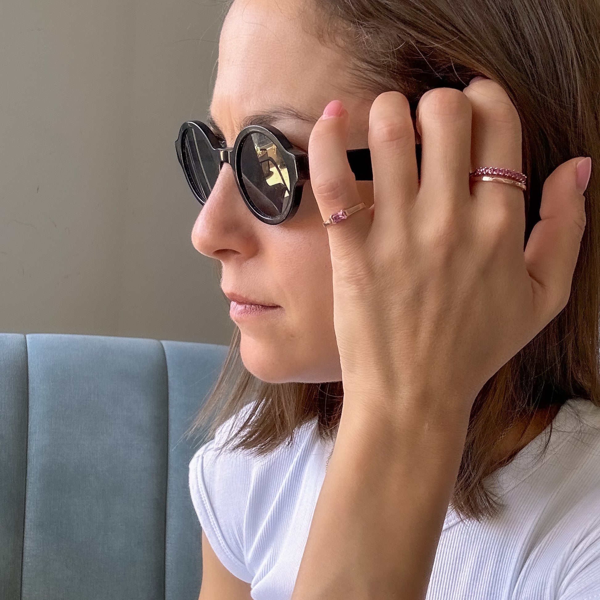 women with sunglasses and white shirt stroking her hair with hand. on her hand  three rose gold rings with natural pink sapphires in a modern geometric design 