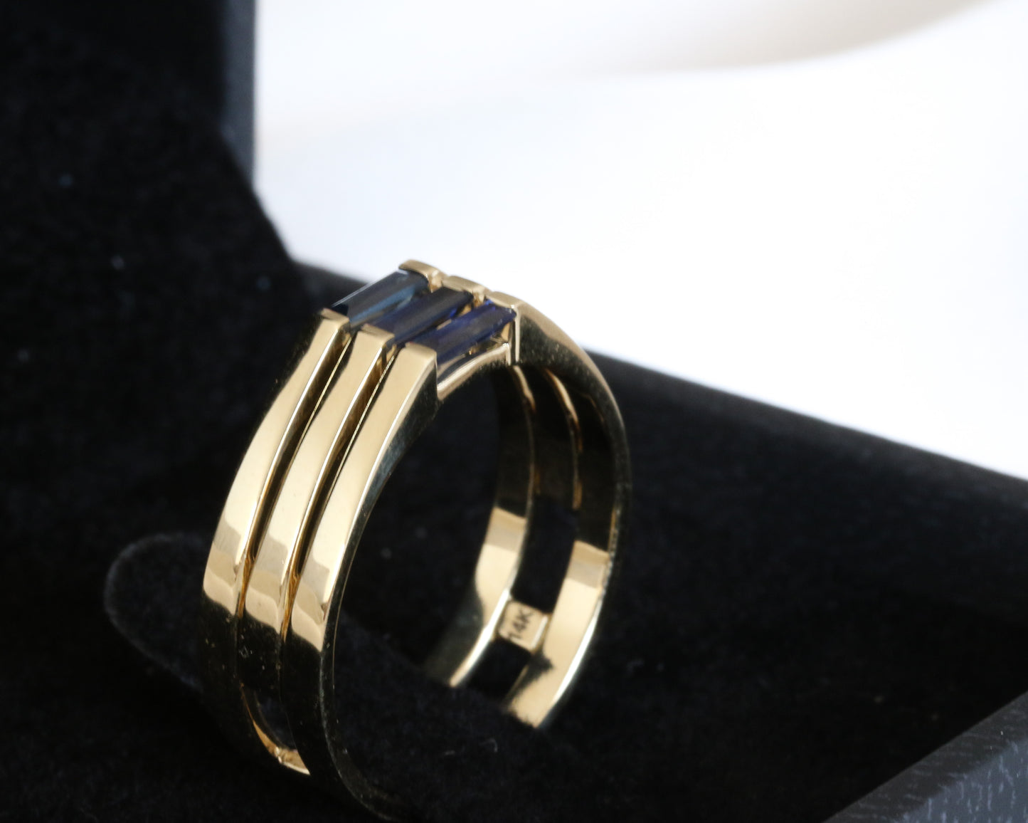A minimalist gold ring with three blue baguette cut sapphires set close together, creating a light and unique appearance shown in black jewelry box