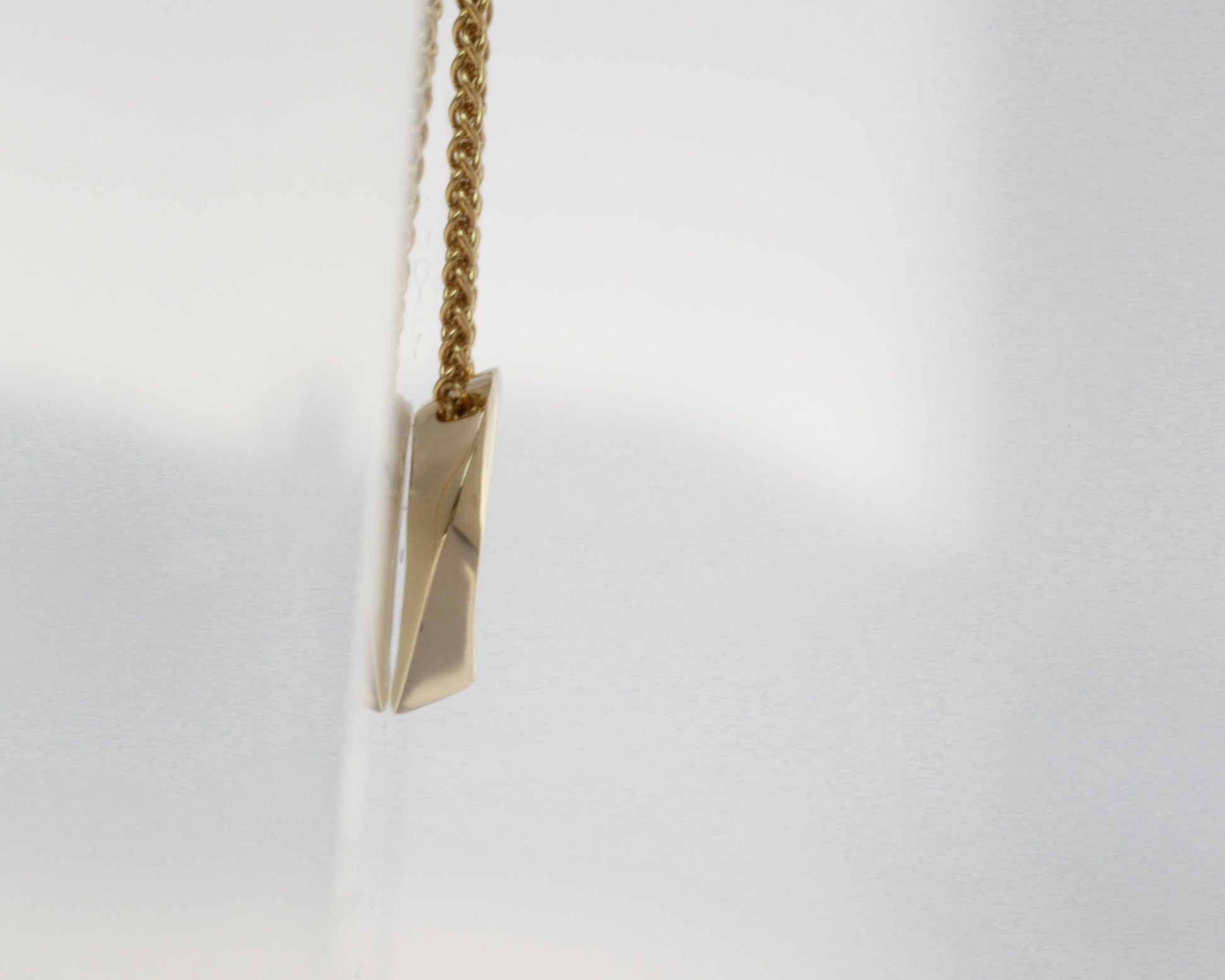 Gold necklace with a geometric pendant on a light gray background