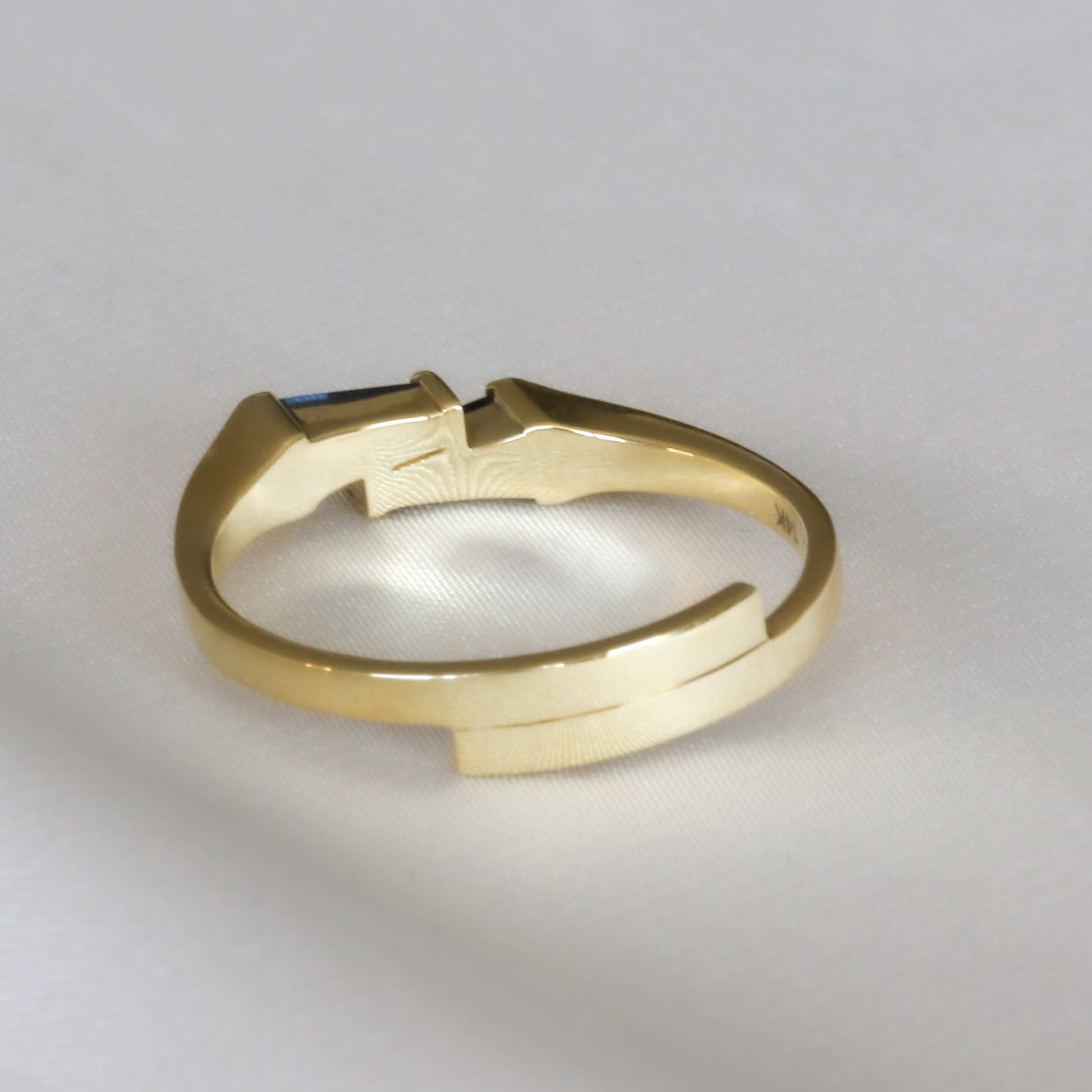 A gold ring with two blue sapphires set cheek to cheek shown from the back