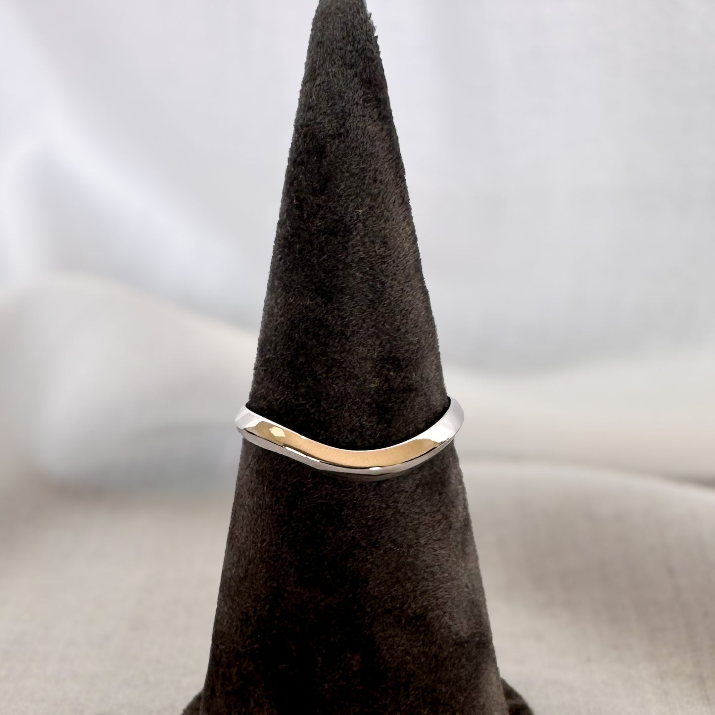 A 14K gold ring with a modern geometric wavy design, sitting on a textured surface.