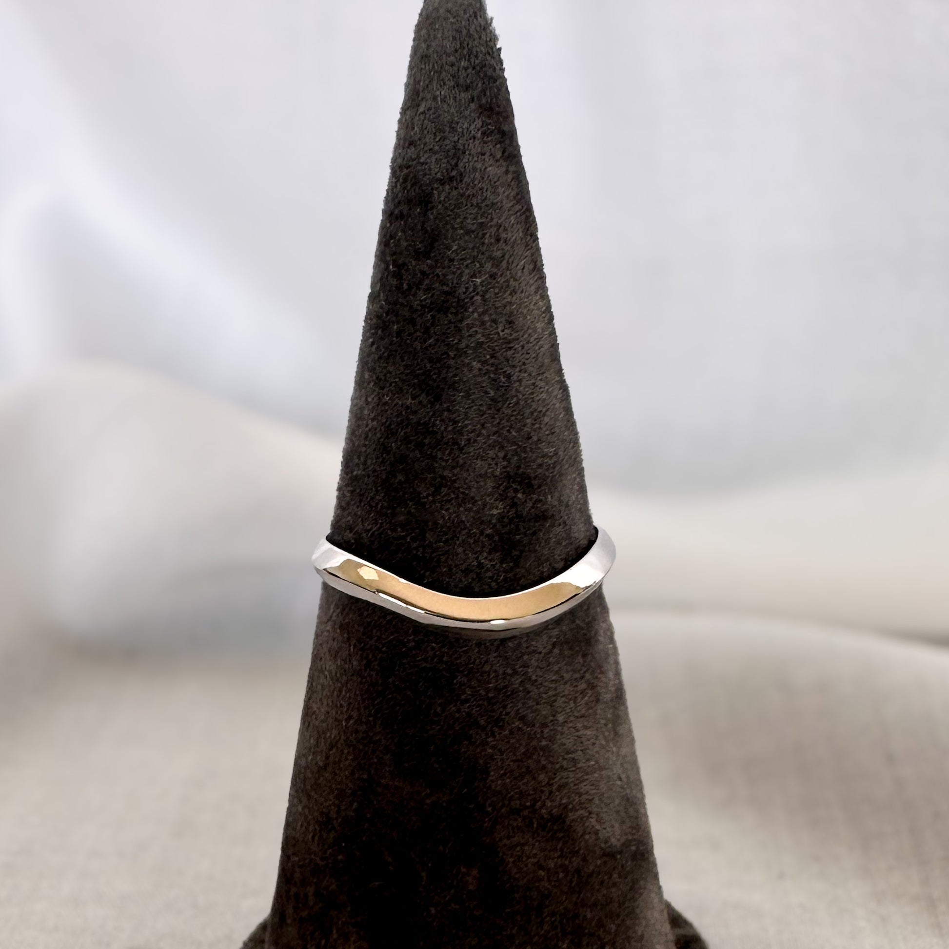A 14K gold ring with a modern geometric wavy design, sitting on a textured surface.