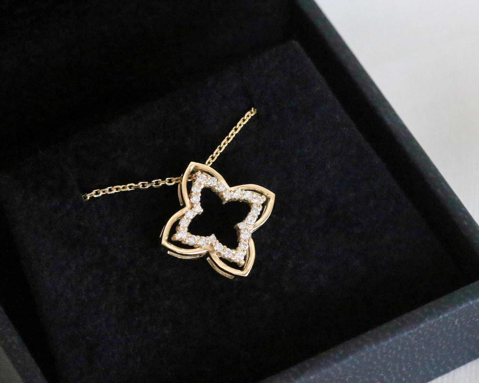 Gold necklace with a clover-shaped pendant on a dark fabric surface