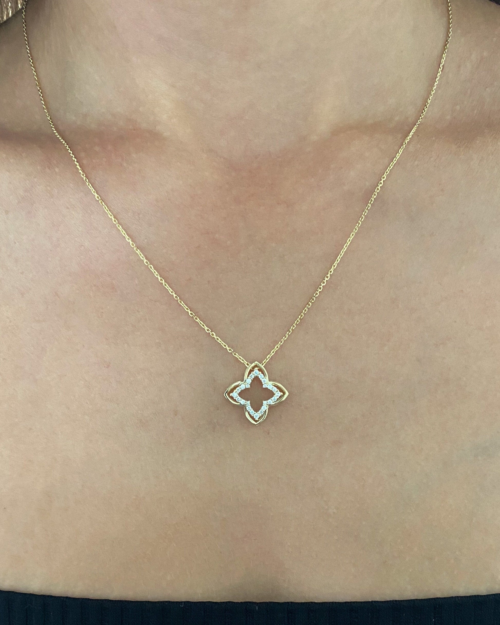 Gold necklace with a clover-shaped pendant on a person's neck