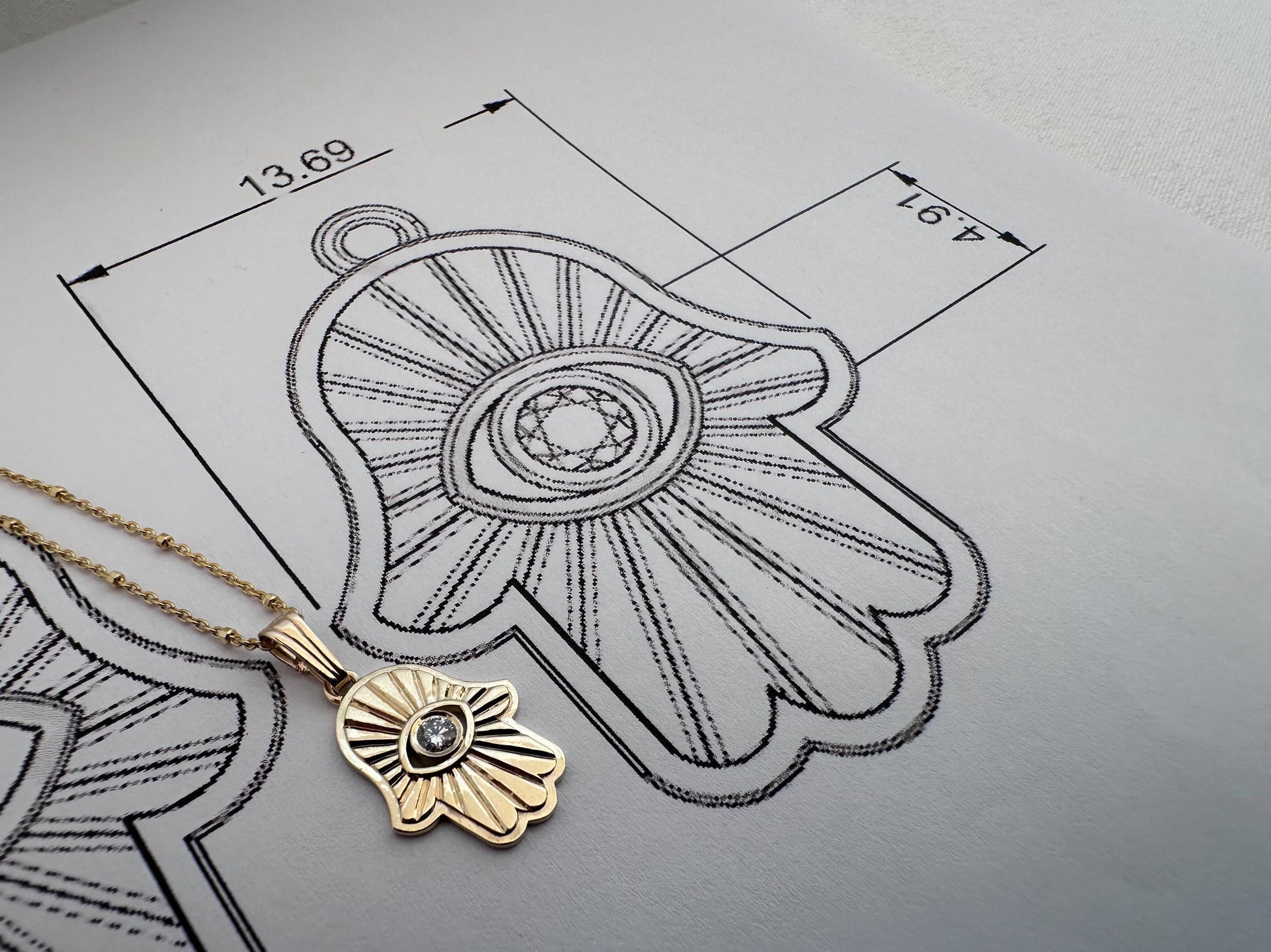 Gold pendant on a gray surface with technical drawing and measurements