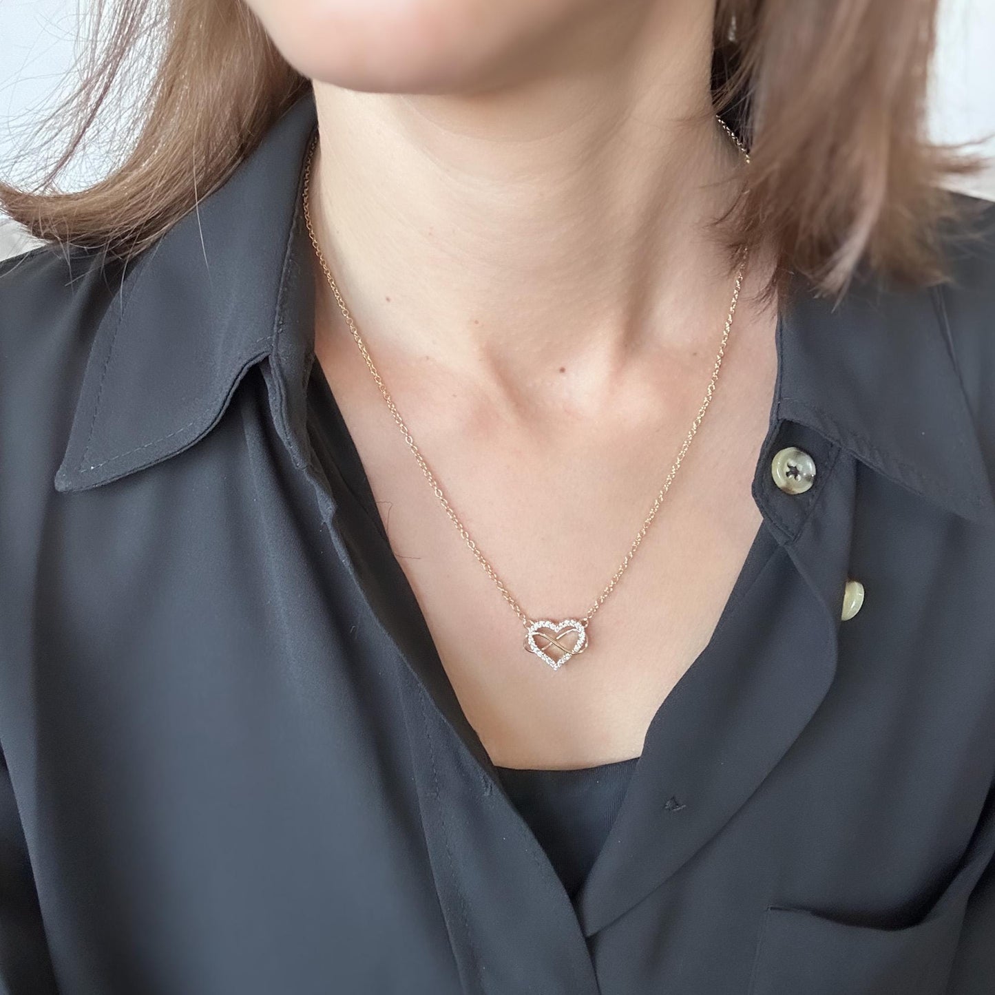 Person wearing a delicate necklace with a heart-shaped pendant on a plain background
