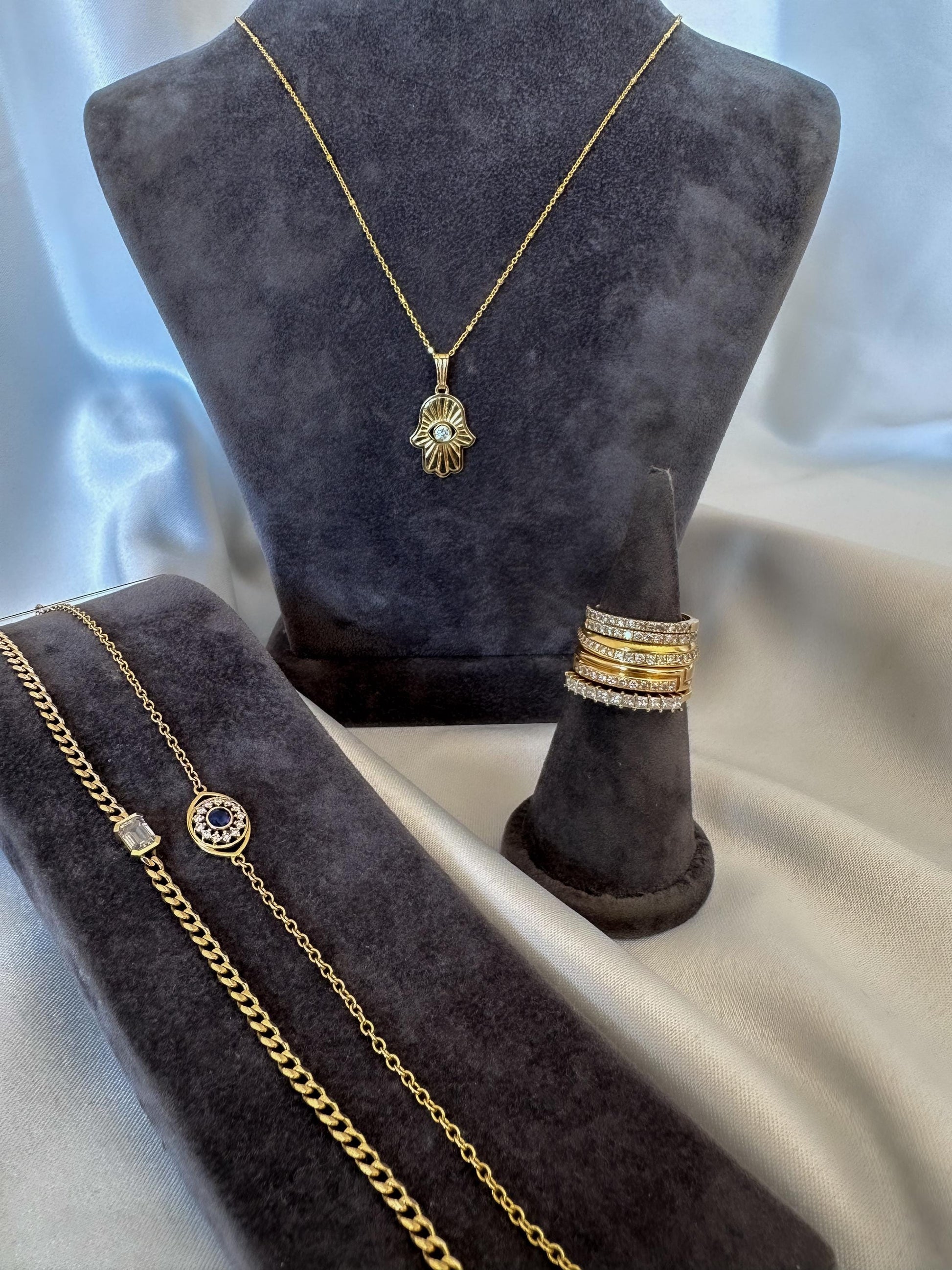Gold jewelry set including necklace, bracelet, and rings on a gray velvet stand.