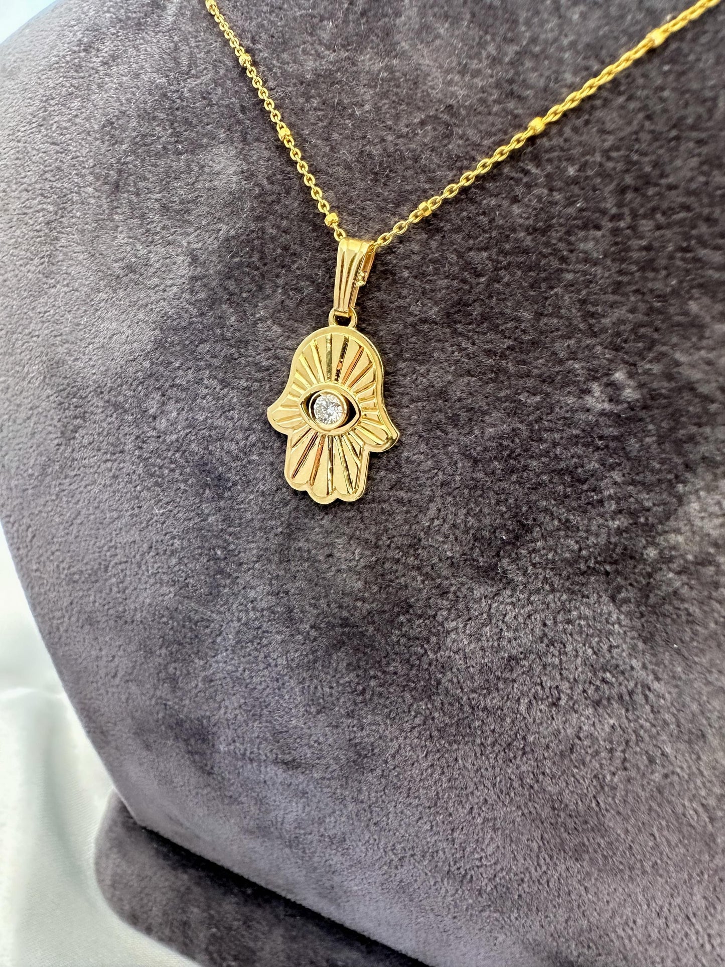 Gold Hamsa hand necklace with a diamond on a gray textured surface