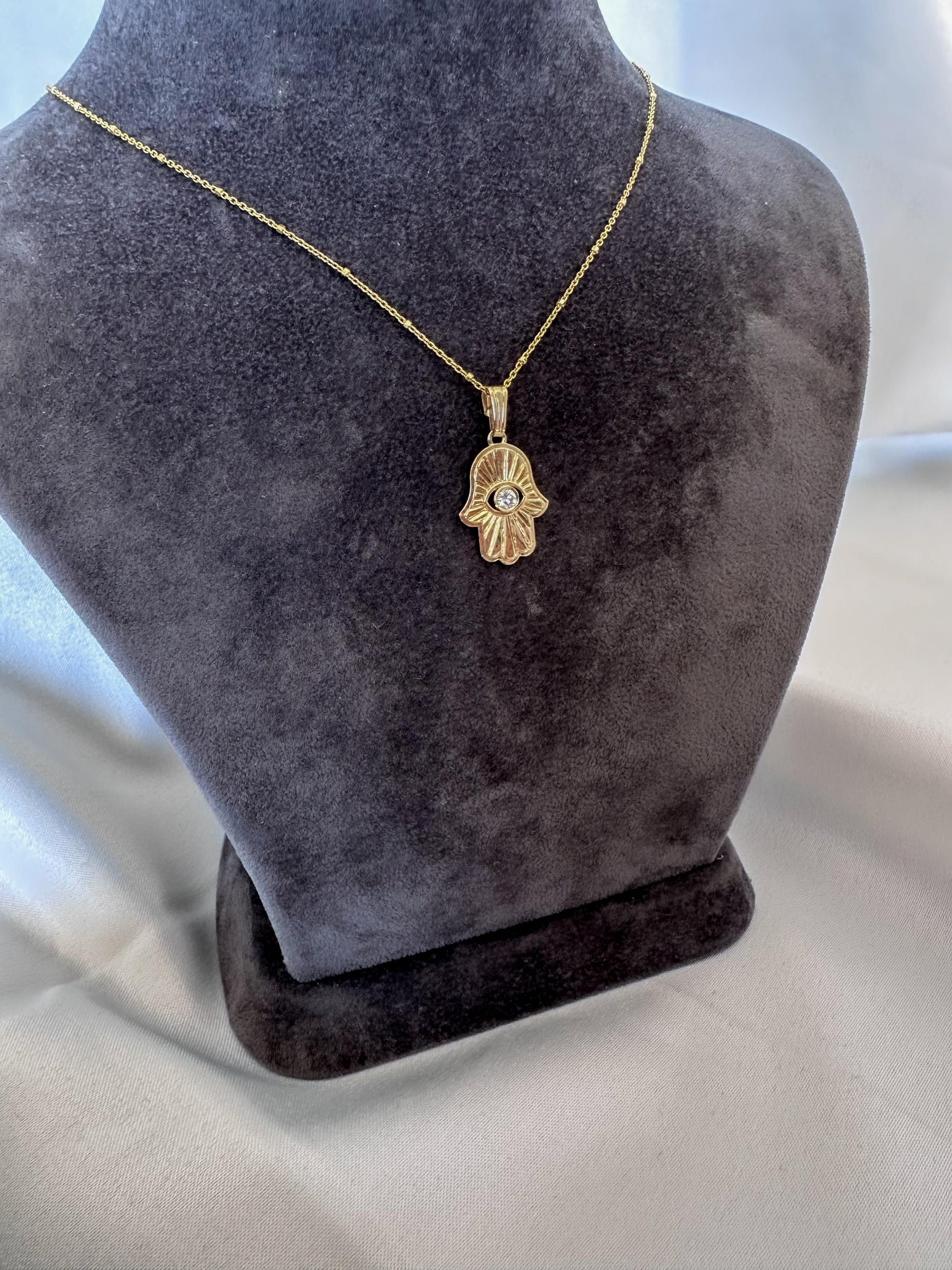 Gold necklace with a hamsa hand pendant on a gray mannequin bust.