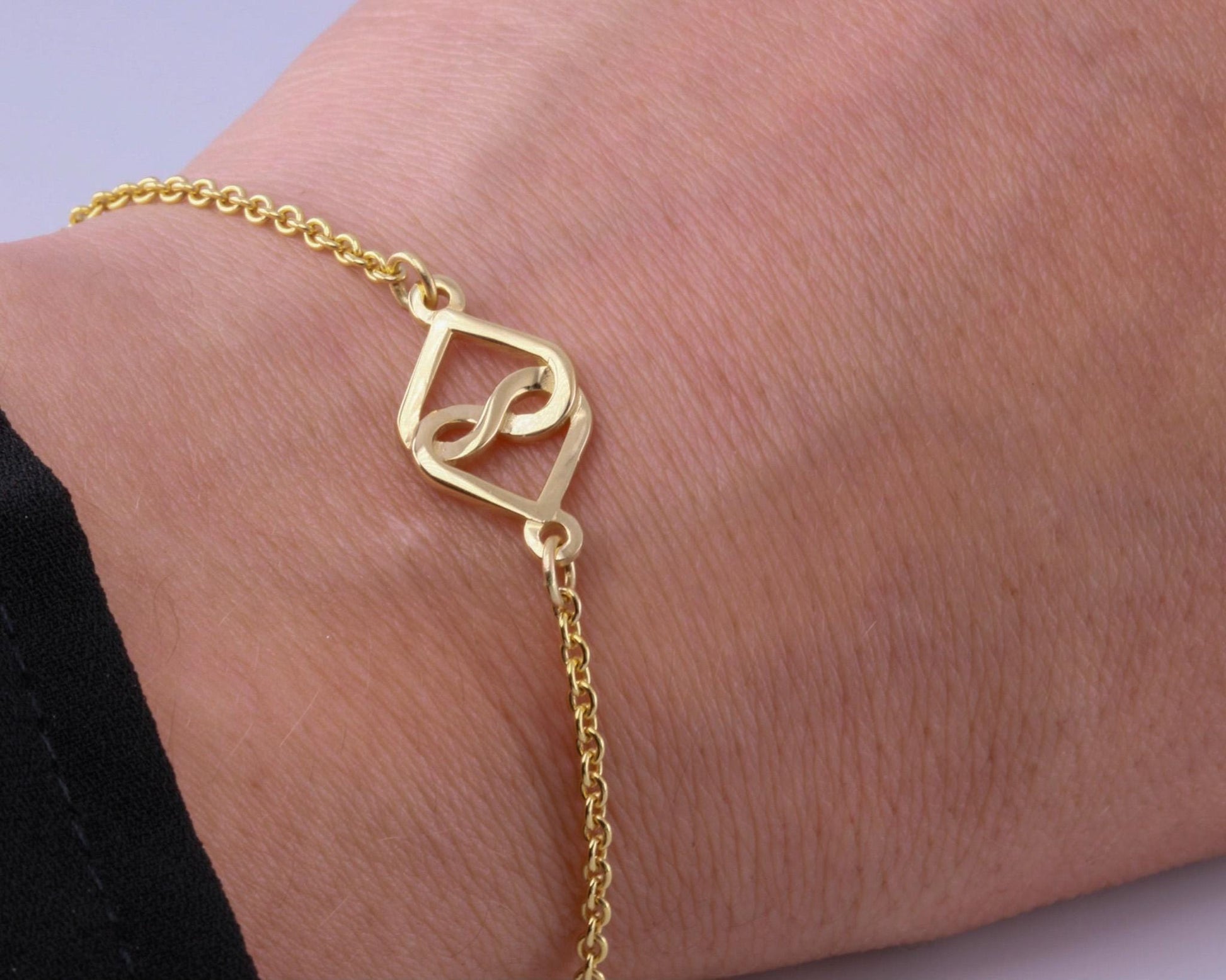 Gold bracelet with a unique design on a wrist against a light purple background