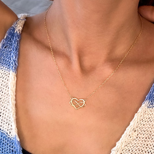Polished 14K yellow gold heart infinity pendant on a rolo chain, worn on the neck, close-up