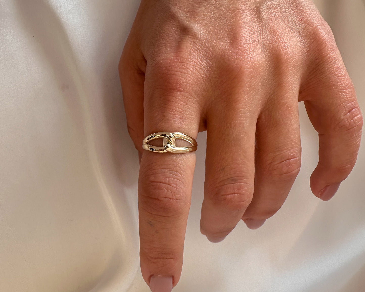 Hand wearing a dainty gold infinity knot ring