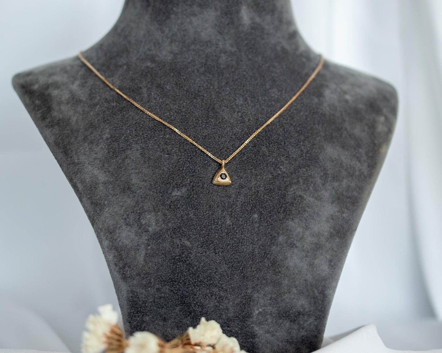 Gold sapphire triangle pendant necklace on a display bust with dried flowers