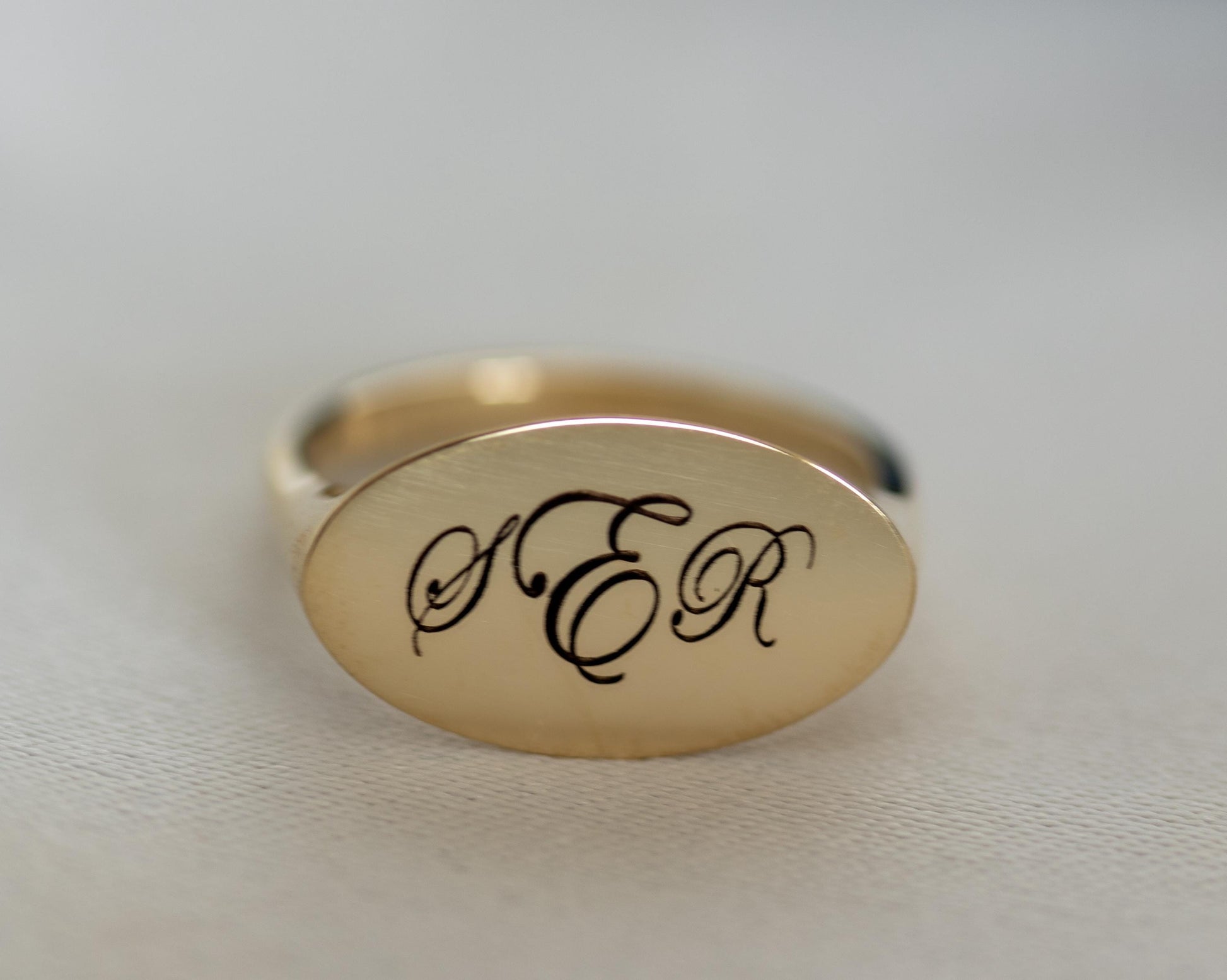 Gold ring with 'ER' engraving on a light gray background