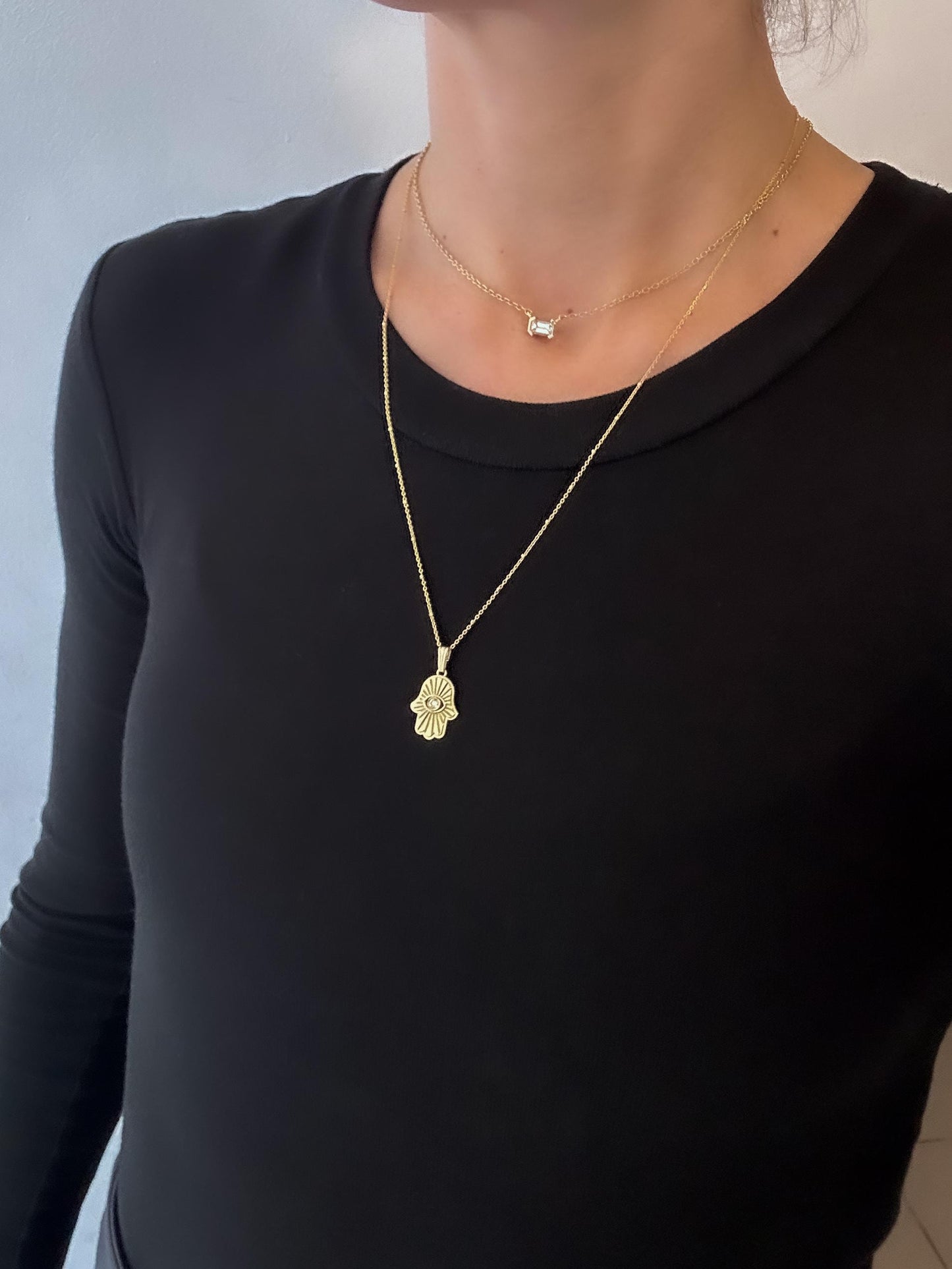 Person wearing a black long-sleeve top with a gold necklace featuring a small pendant.