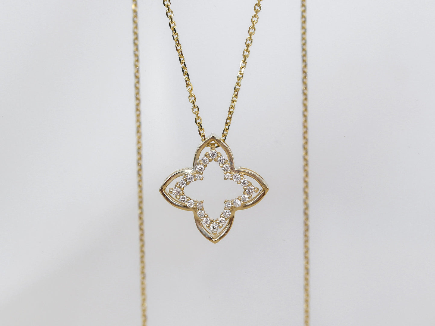 Gold necklace with a clover-shaped pendant on a light gray background