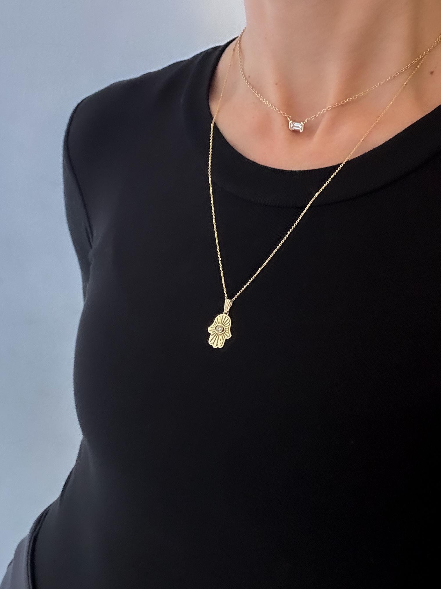 Gold necklace with a hamsa pendant worn by a person against a plain background