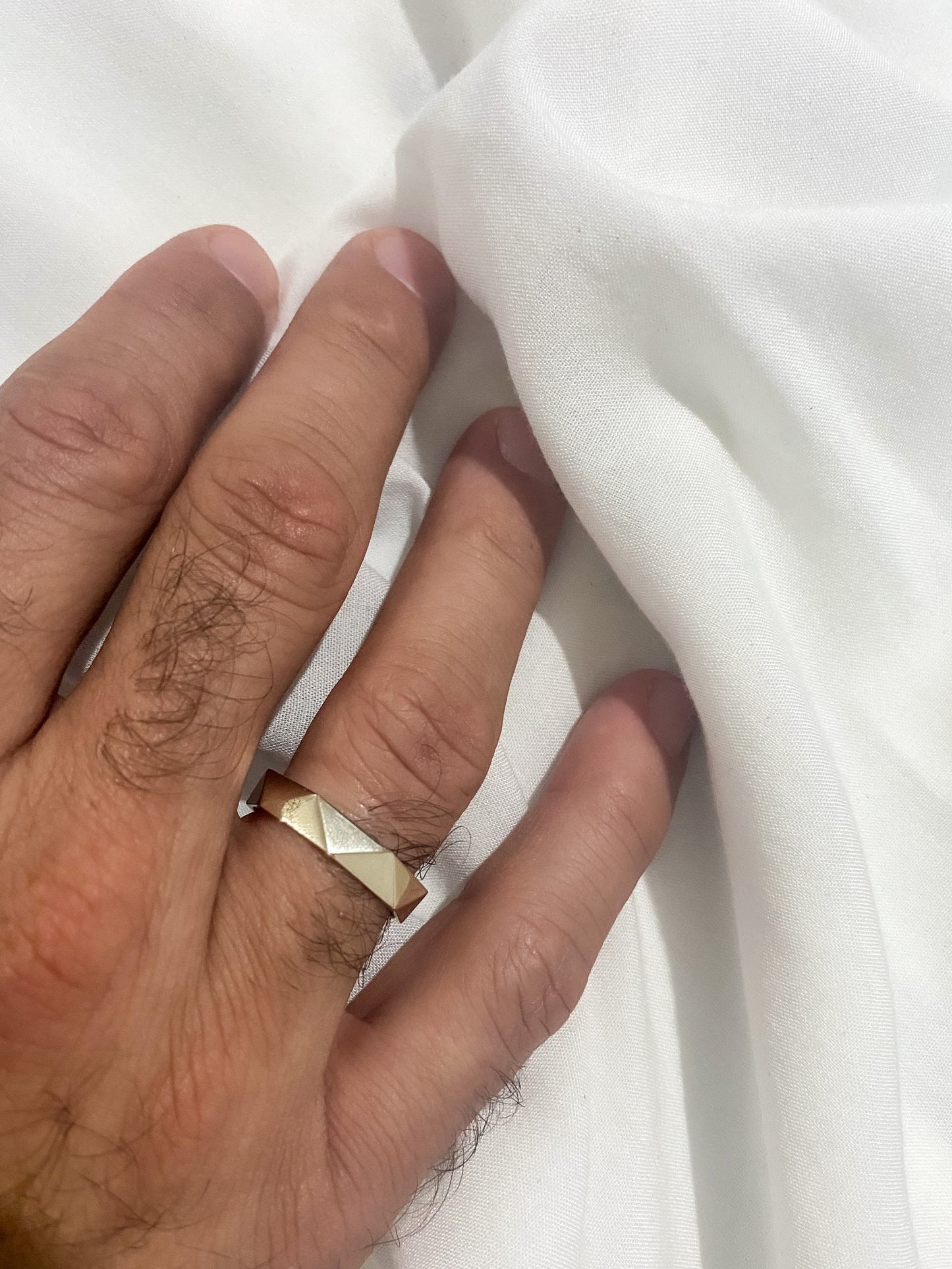 hand wearing faceted gold band on white fabric