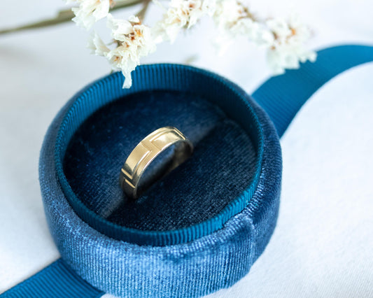 hand wearing wide carved gold band on dark background