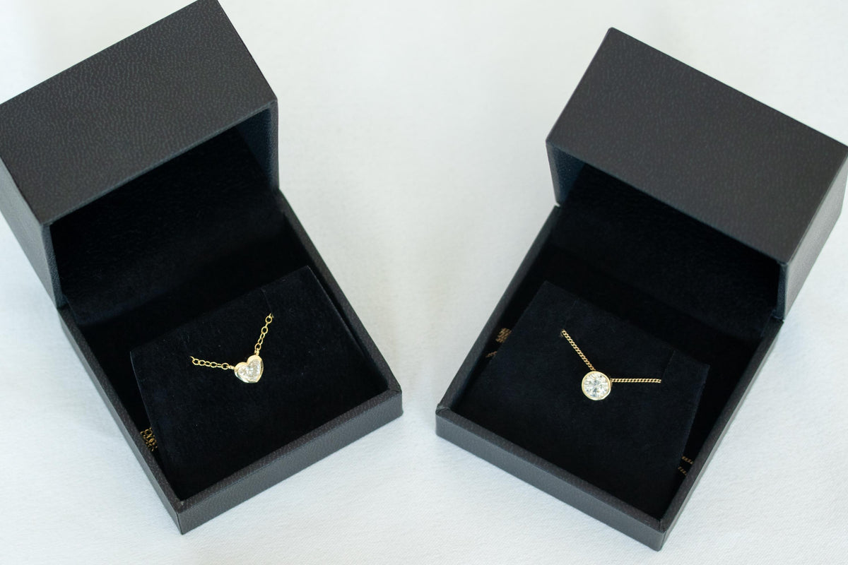 Heart shape diamond necklace and round diamond bezel necklace in 14K yellow gold, in black jewelry boxes