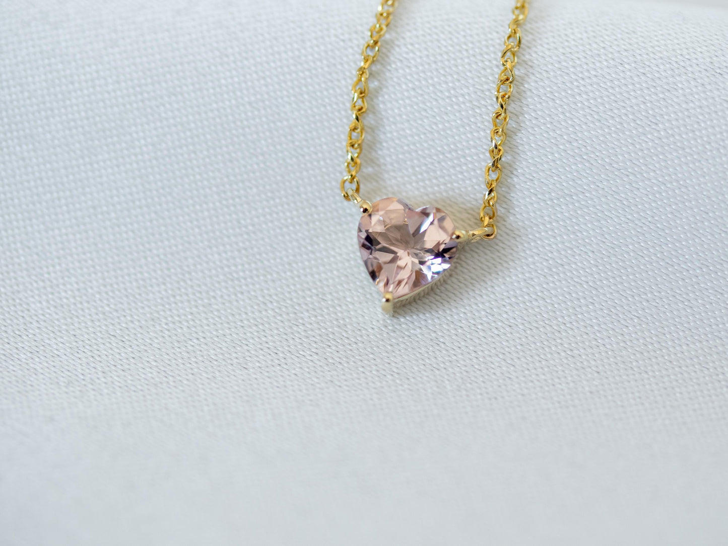 Heart-shaped pink gemstone necklace on a gold chain against a light gray background