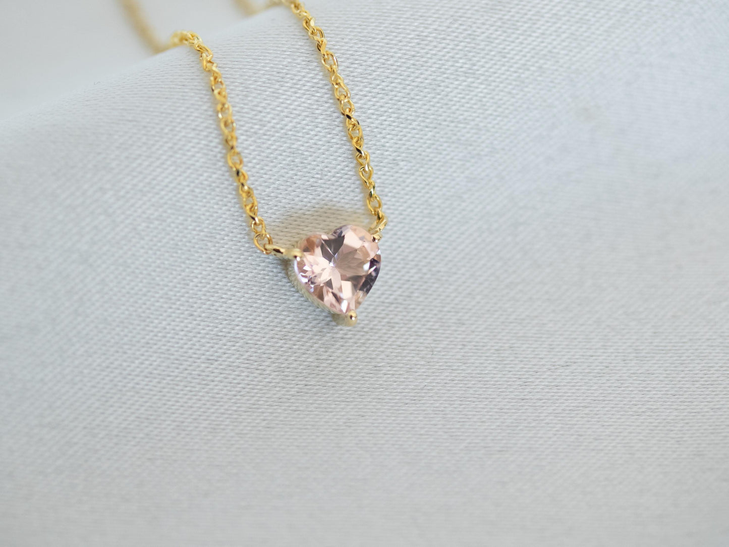 Gold necklace with a heart-shaped pink gemstone on a light gray background
