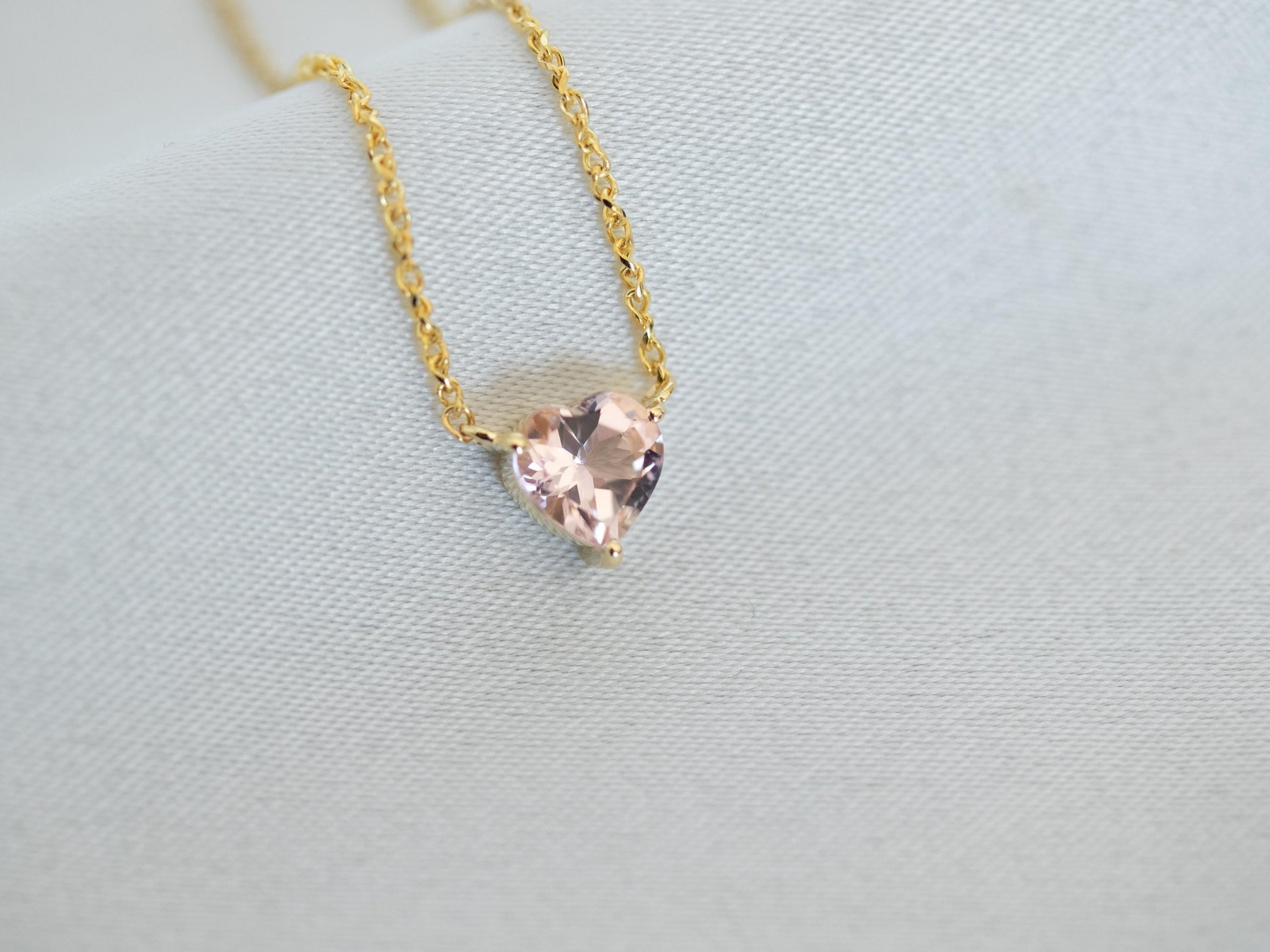 Gold necklace with a heart-shaped pink gemstone on a light gray background