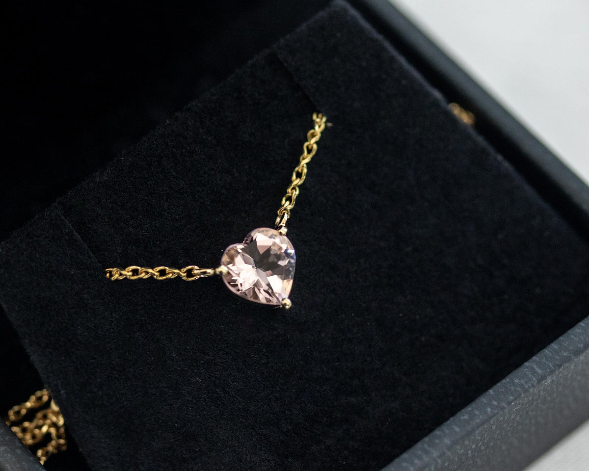 Close-up of a prong-set heart shape morganite on a 14K yellow gold rolo chain in a jewelry box