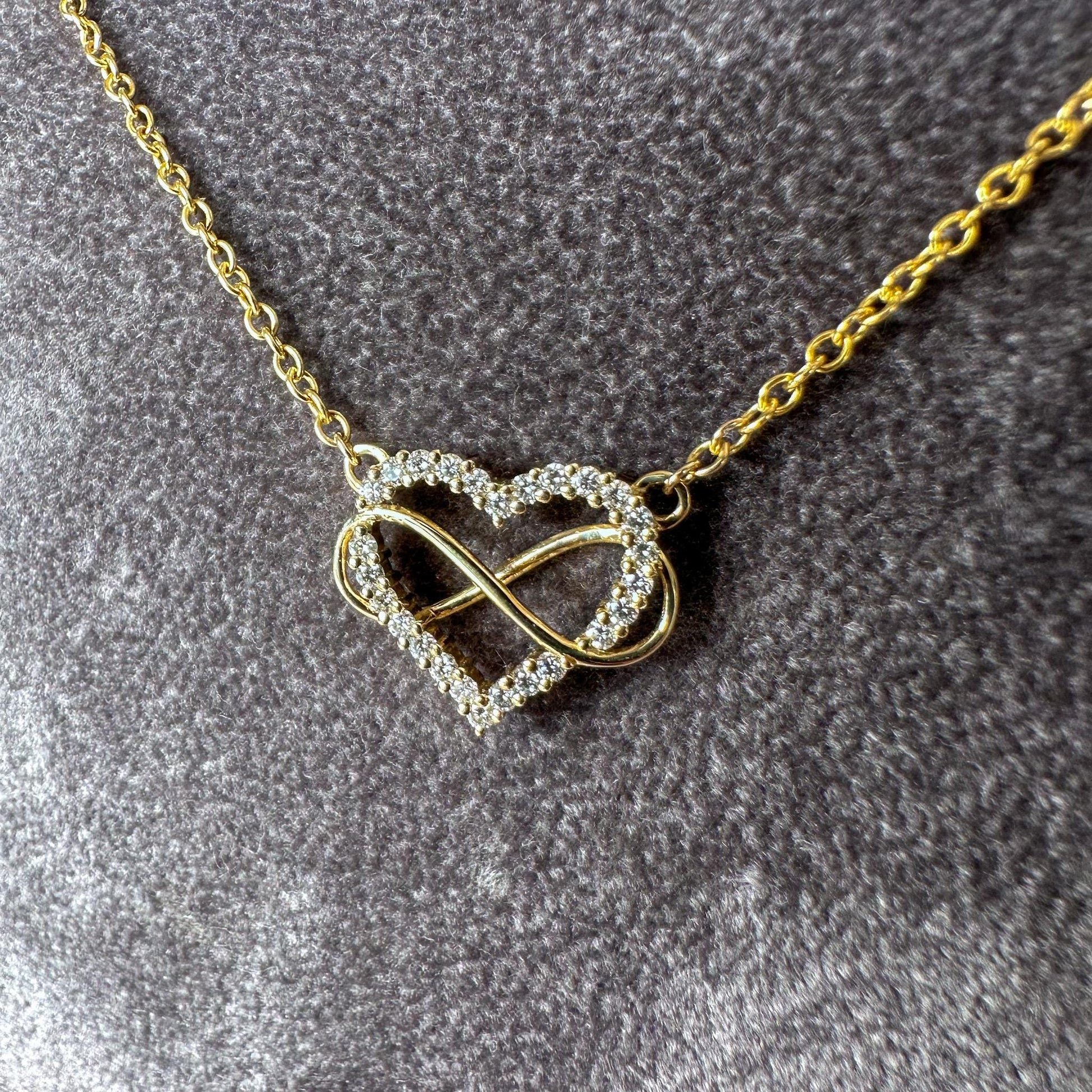 Gold necklace with a heart and infinity symbol pendant on a gray textured background