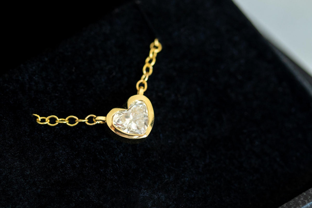 Close-up of a heart shape diamond in a 14K yellow gold bezel, with the rolo chain attached on both sides