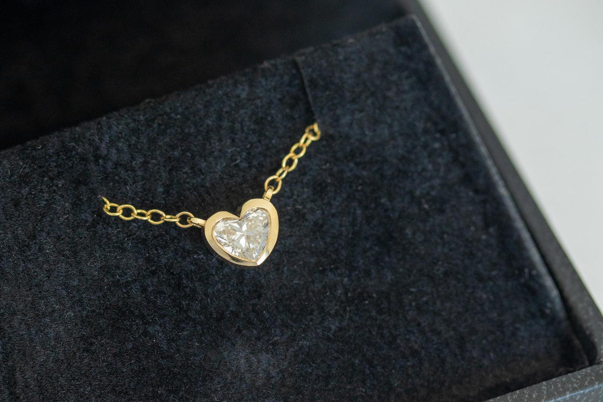 Heart shape diamond in a 14K yellow gold bezel, angled close-up on black velvet