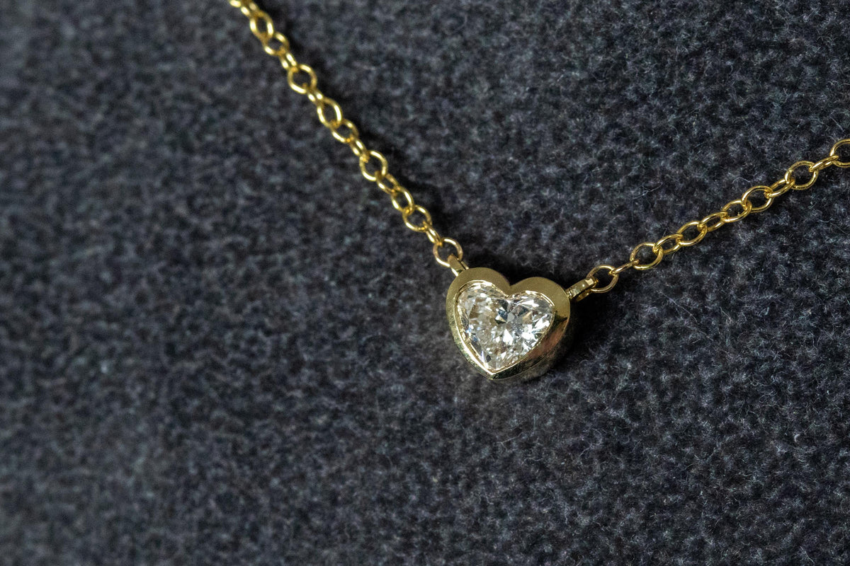 Heart shape diamond bezel necklace in 14K yellow gold, front view on gray velvet
