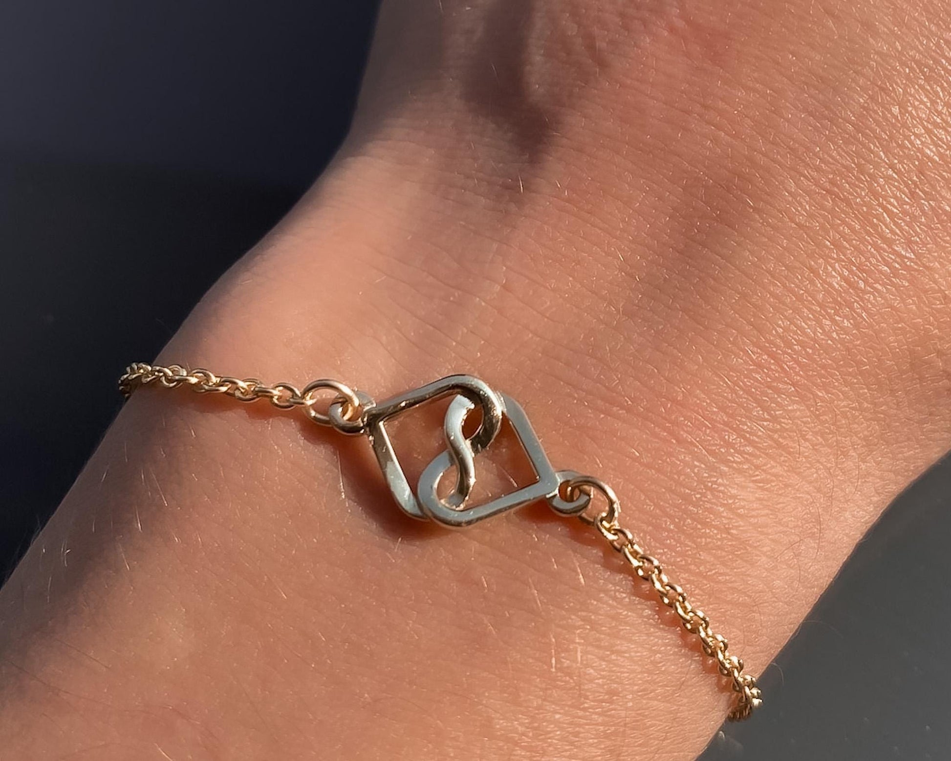 Gold bracelet with a heart-shaped clasp on a wrist against a dark background