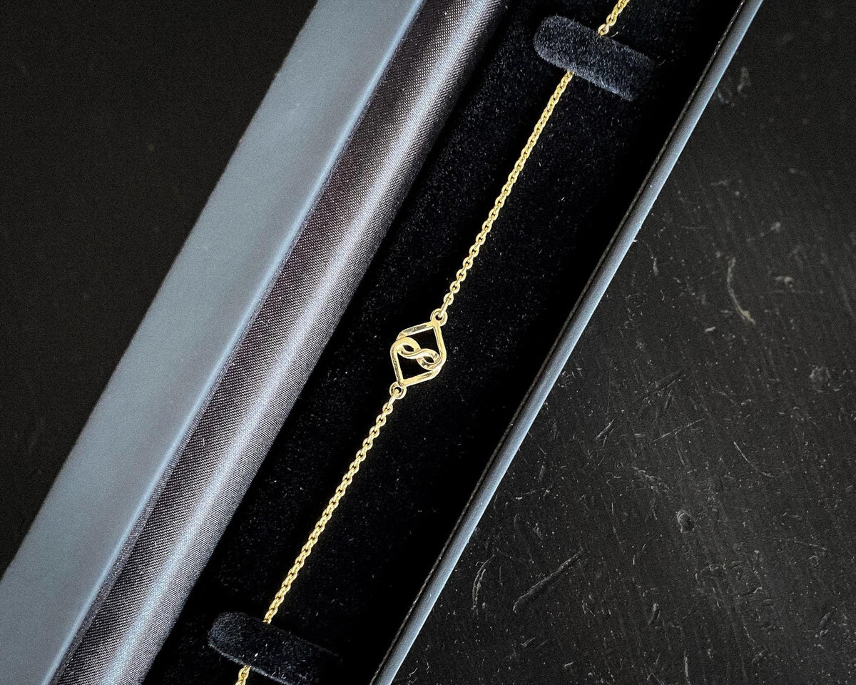 14K yellow gold infinity heart bracelet in a black jewelry box, angled view