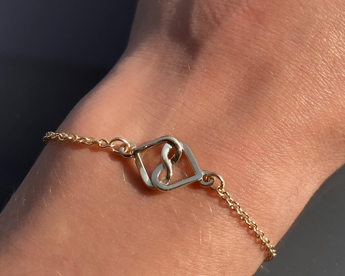14K yellow gold infinity heart bracelet worn on the wrist against a dark background