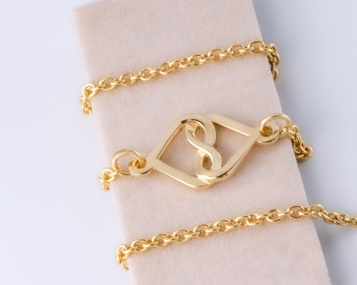14K yellow gold infinity heart charm bracelet wrapped around a display block