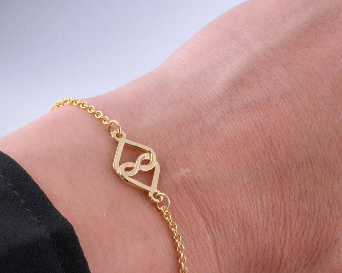 14K yellow gold rolo chain bracelet with an infinity heart charm on the wrist, side view