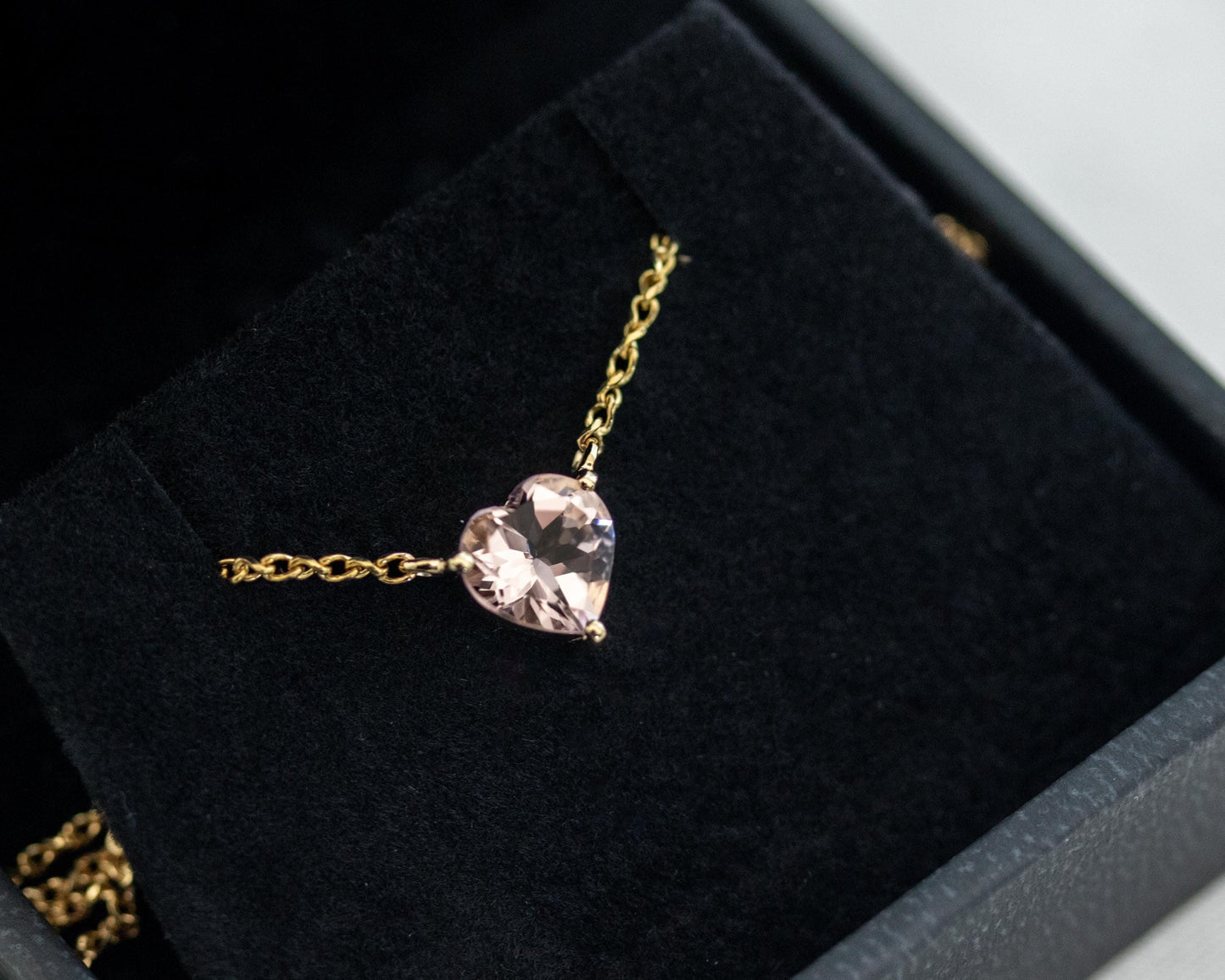 Gold necklace with a pink heart-shaped pendant on a black velvet surface