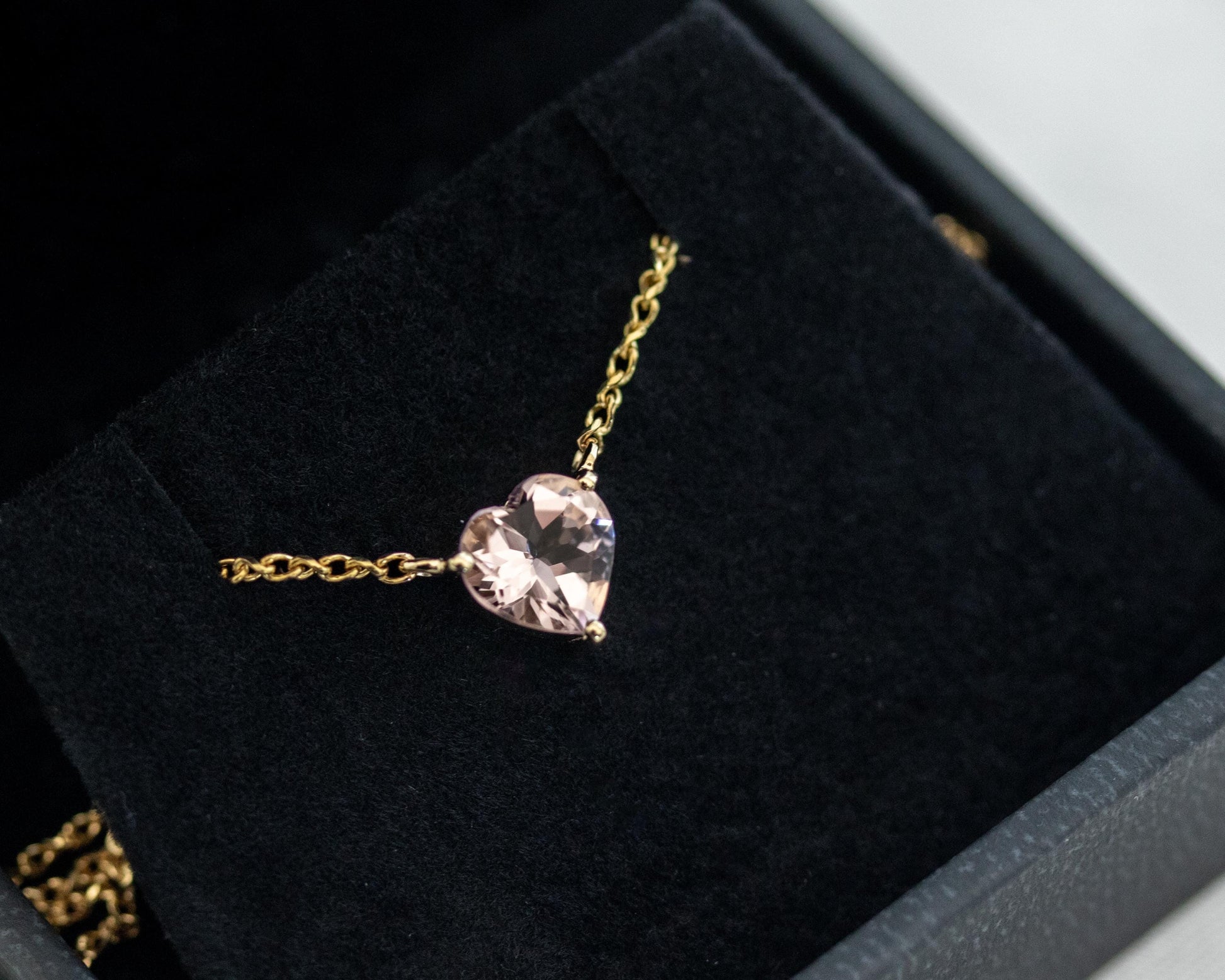 Gold necklace with a pink heart-shaped pendant on a black velvet surface