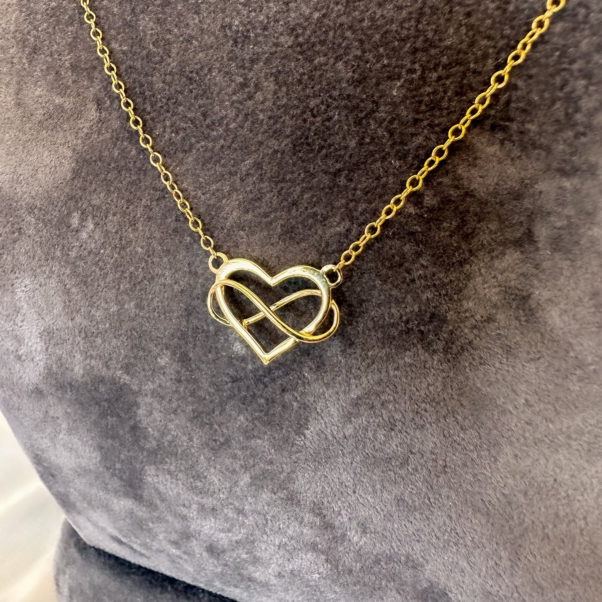 close up yellow gold heart and infinity symbol pendant and chain on gray velvet tourso