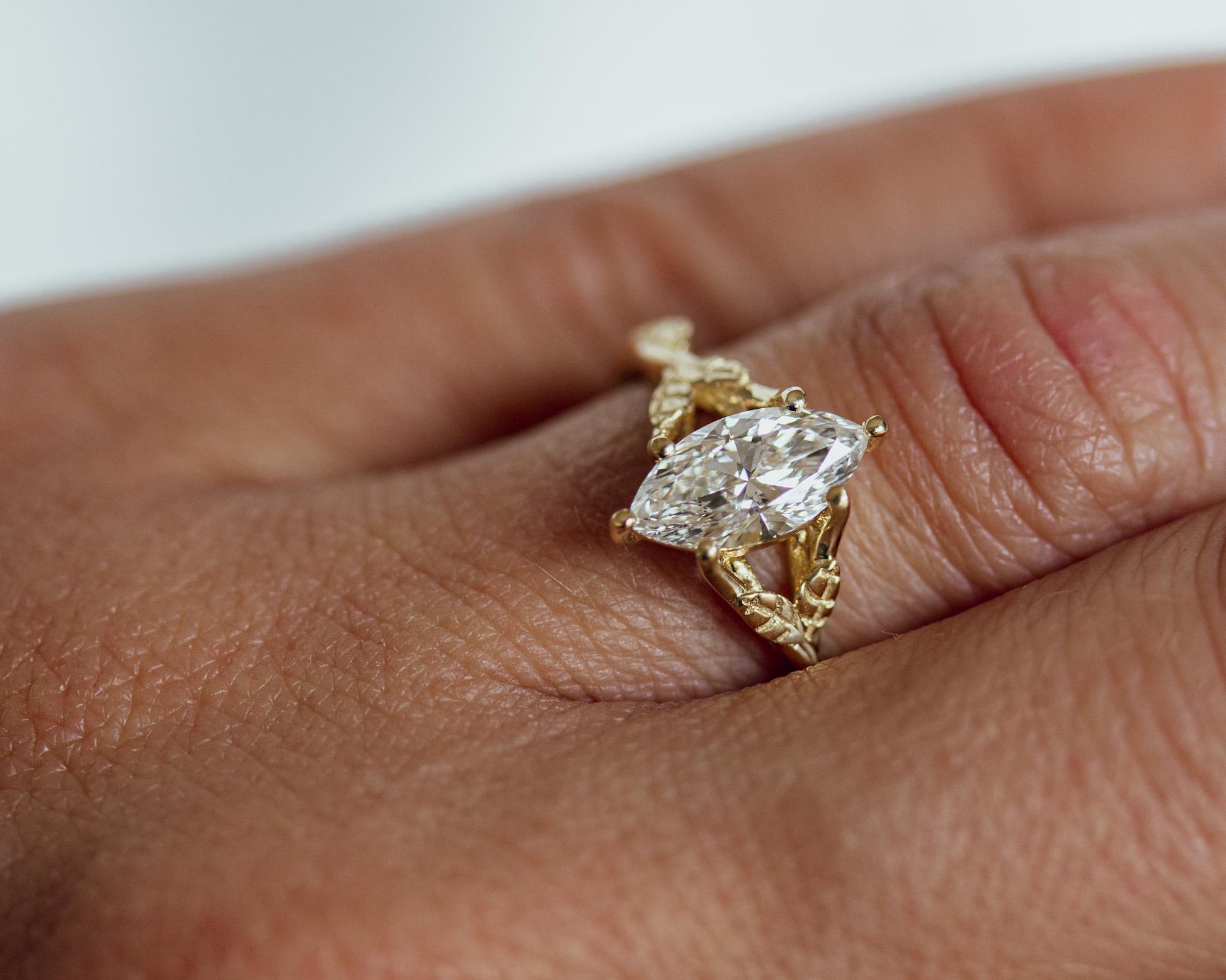 Gold ring with a diamond on a person's finger against a neutral background
