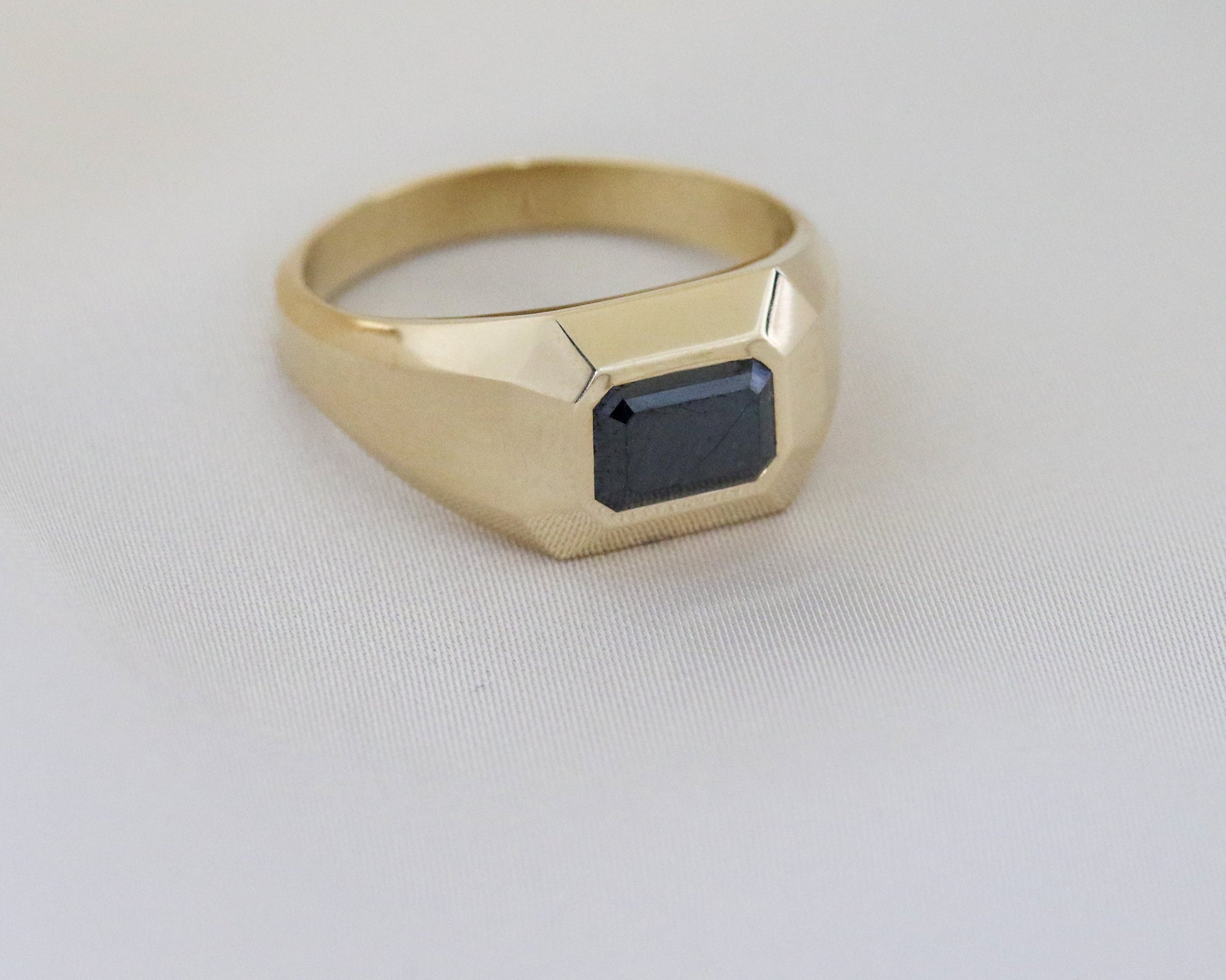 14K gold men’s signet ring with an emerald-cut black diamond on a light background.