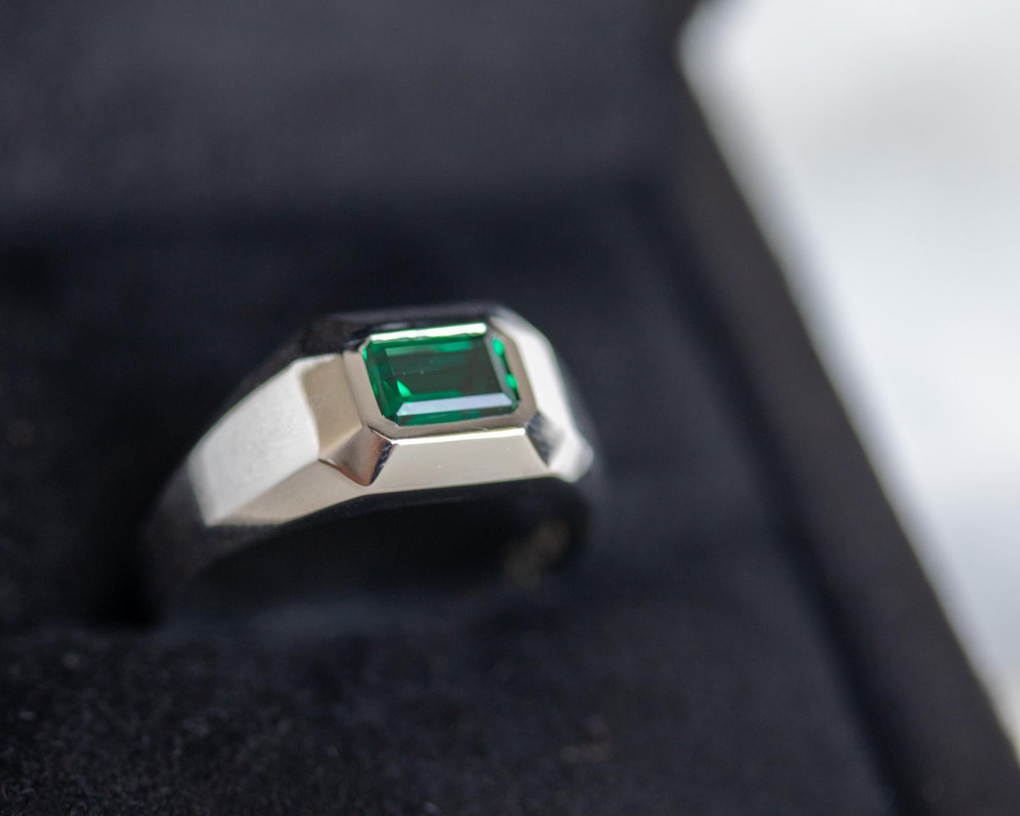 White gold emerald signet ring in a black jewelry box, geometric modern design