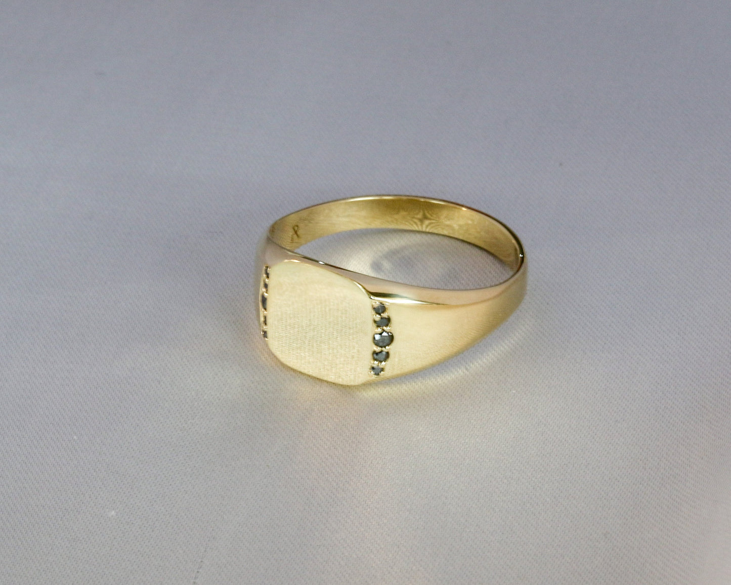 Men’s 14K gold signet ring with black diamonds set along the sides, shown from an angled front view on a light gray background.