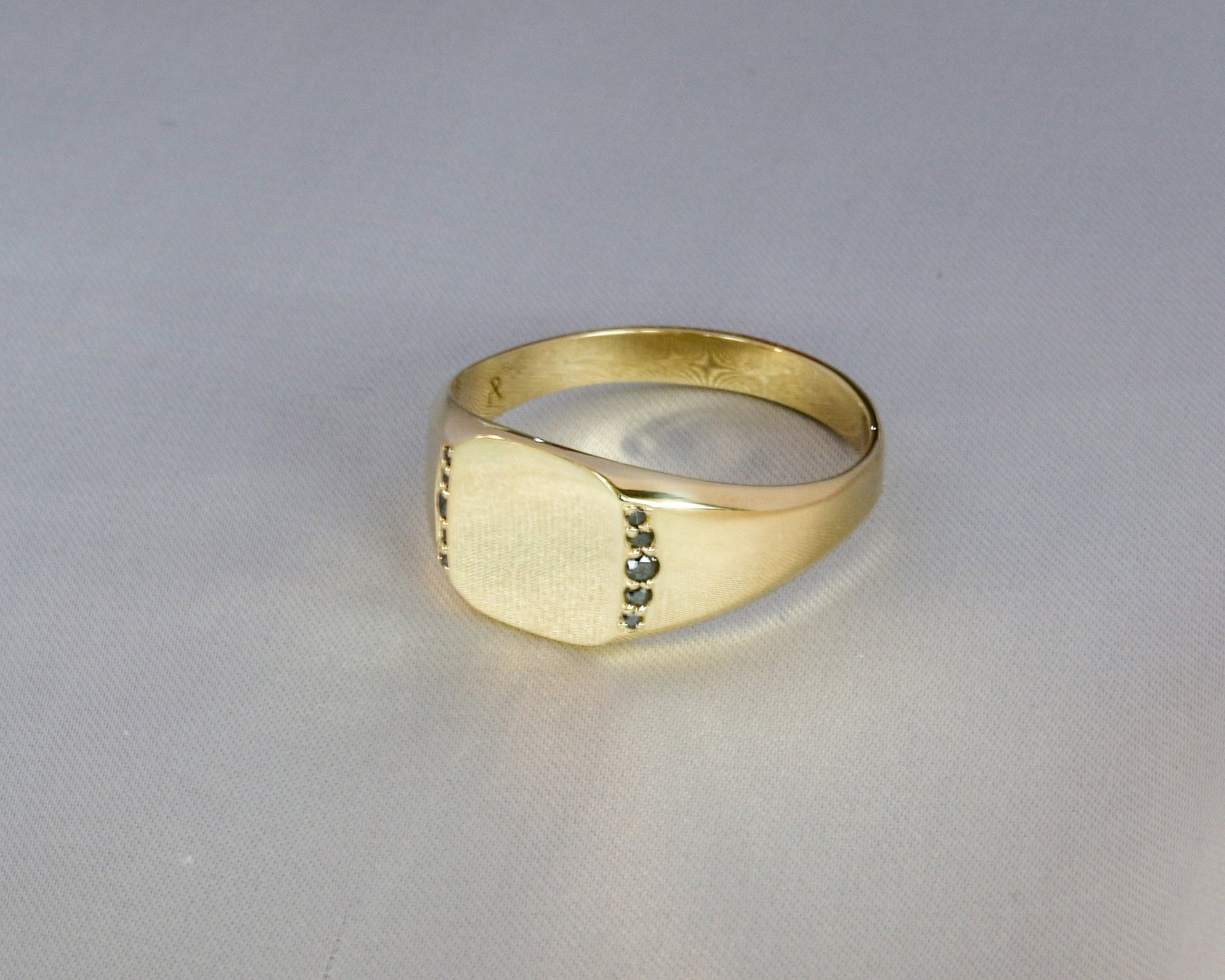 Men’s 14K gold signet ring with black diamonds set along the sides, shown from an angled front view on a light gray background.