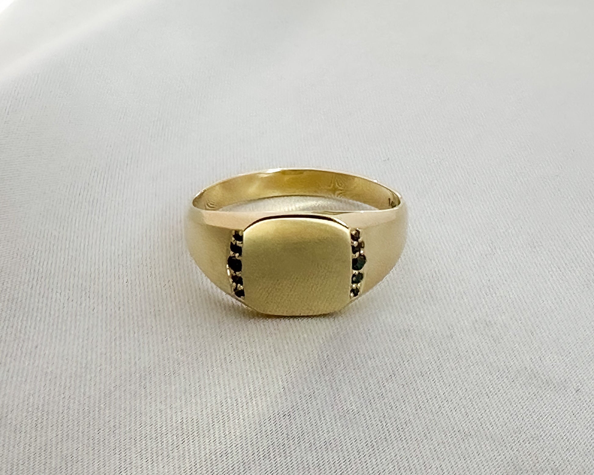 Men’s 14K gold signet ring with black diamonds set along the sides, shown from a front angle on a light gray background.
